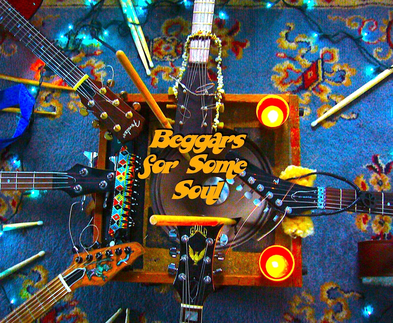 Guitars, drumsticks and candles laid out around an amp, with the Beggars for Some Soul logo at the centre